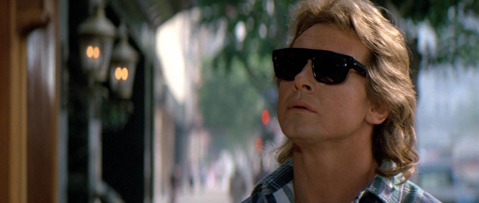 A still frame from the film They Live shows John Nada wearing the sunglasses that let him see the truth behind advertisements. His head is angled slightly upward to give the impression he is looking at the StartRocket image above.